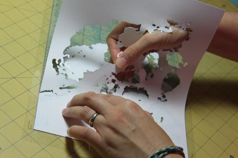 photo of hands pulling the surplus paper from a cut paper artwork