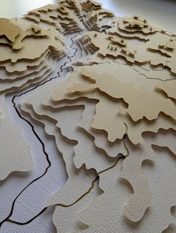 cut and layered paper in shades of white and gold showing topographic elevation