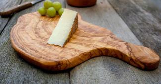 photo of a rustic wooden cheeseboard with a wedge of white cheese and green grapes